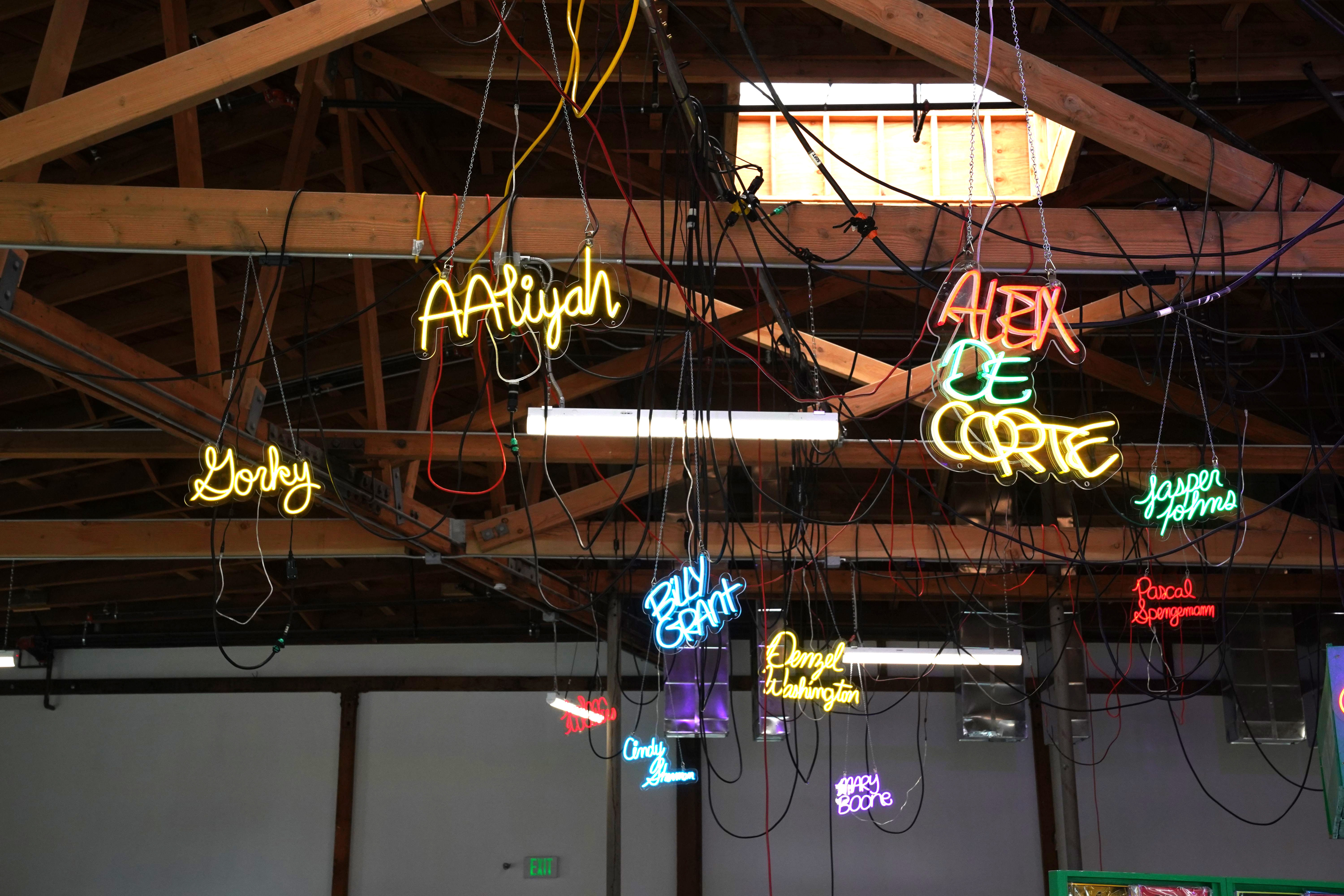 photo of neon signs hanging from the ceiling that have famous poeoples names on them