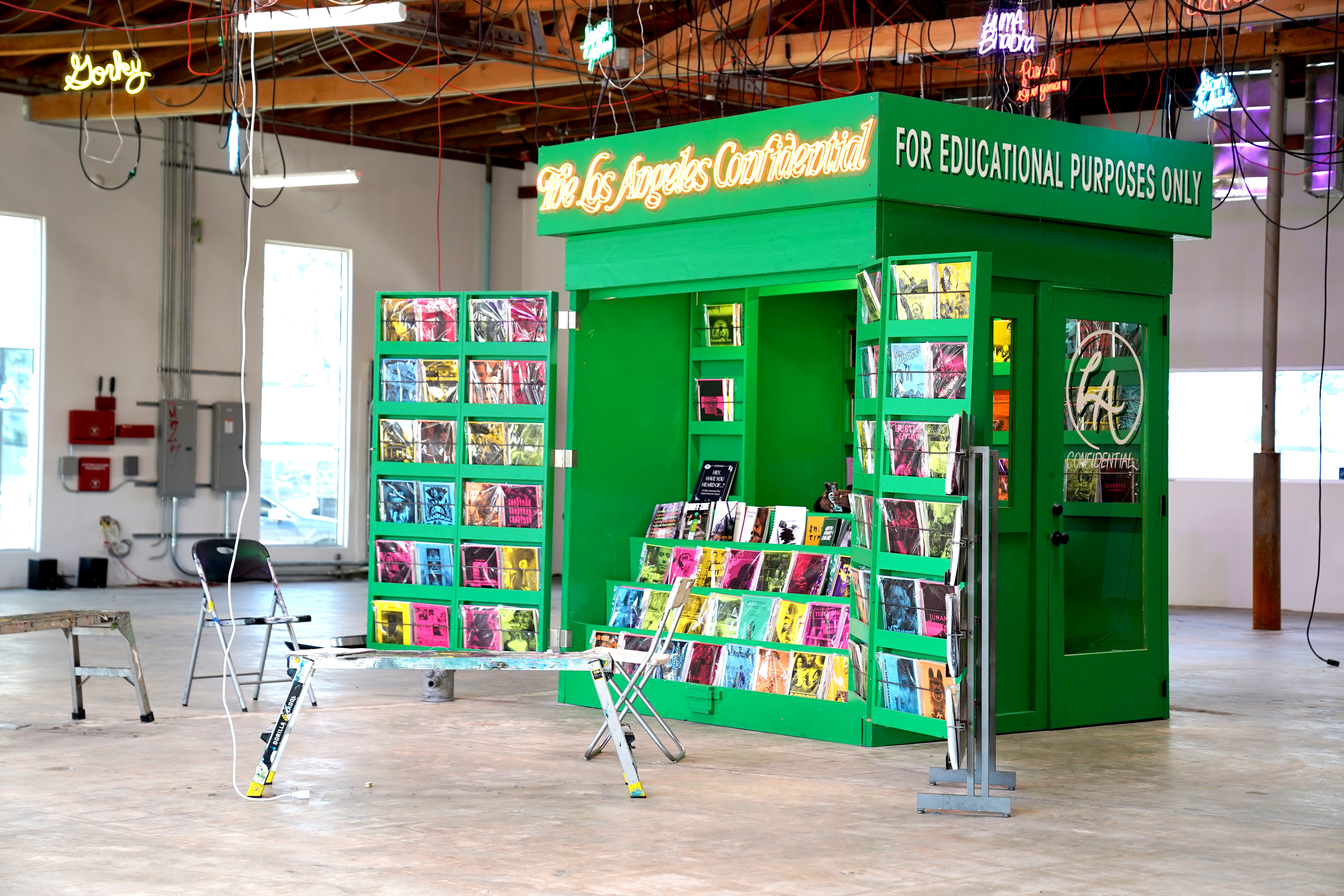 photo of a newsprint stand painted green with neon signs hanging above
