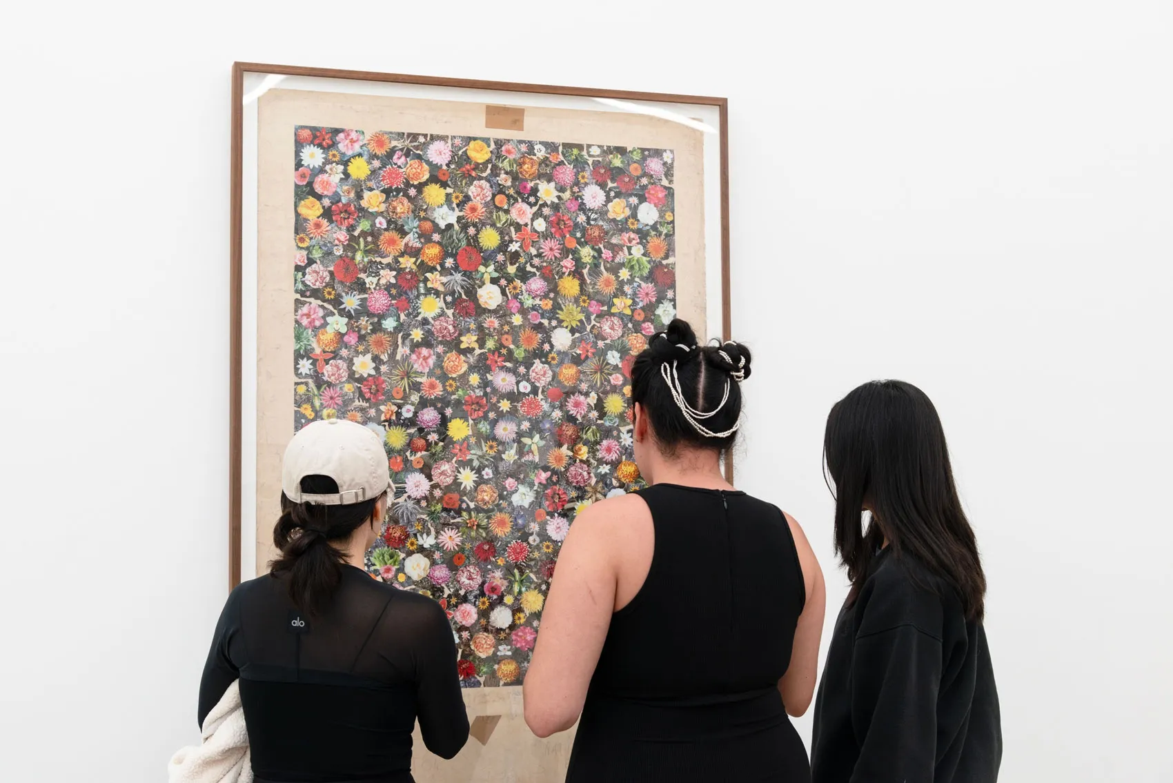 LA DIrector Dasha Matsuura stands in front of a large scale floral collage piece with two attendees of the opening reception. 