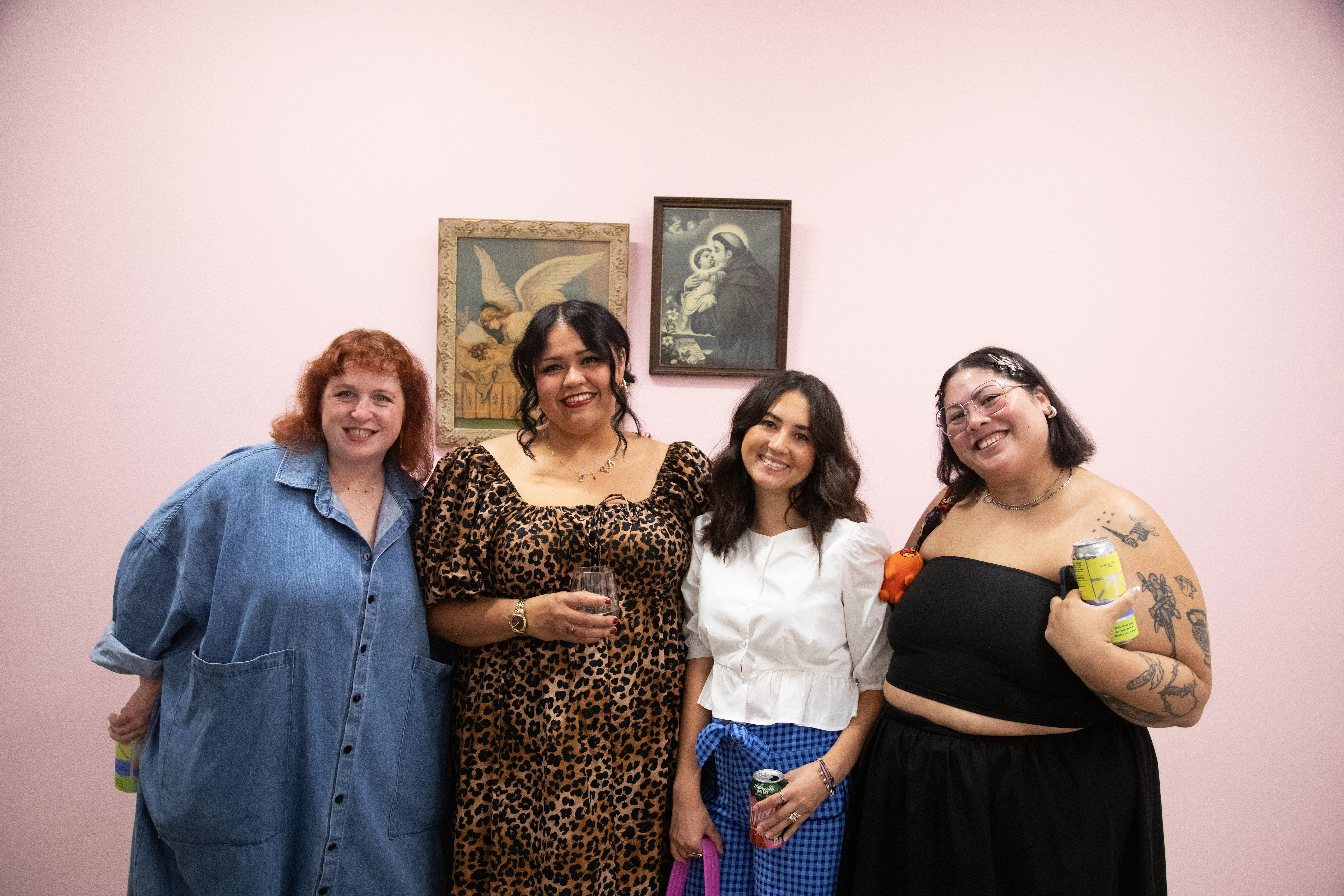 Artist Gina M. Contreras poses with friends in front of her installation on a pink wall in the art gallery.