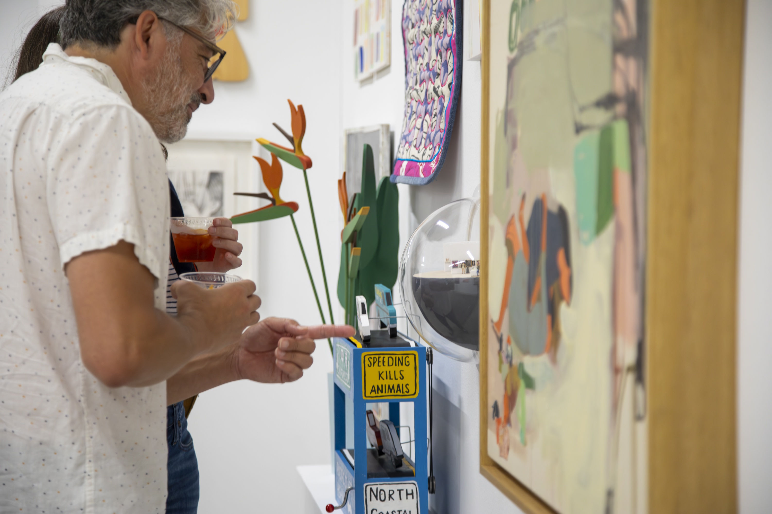 Guests look at paintings and sculptures hanging on a white gallery all at the opening reception of the 10 Year Anniversary group exhibition.
