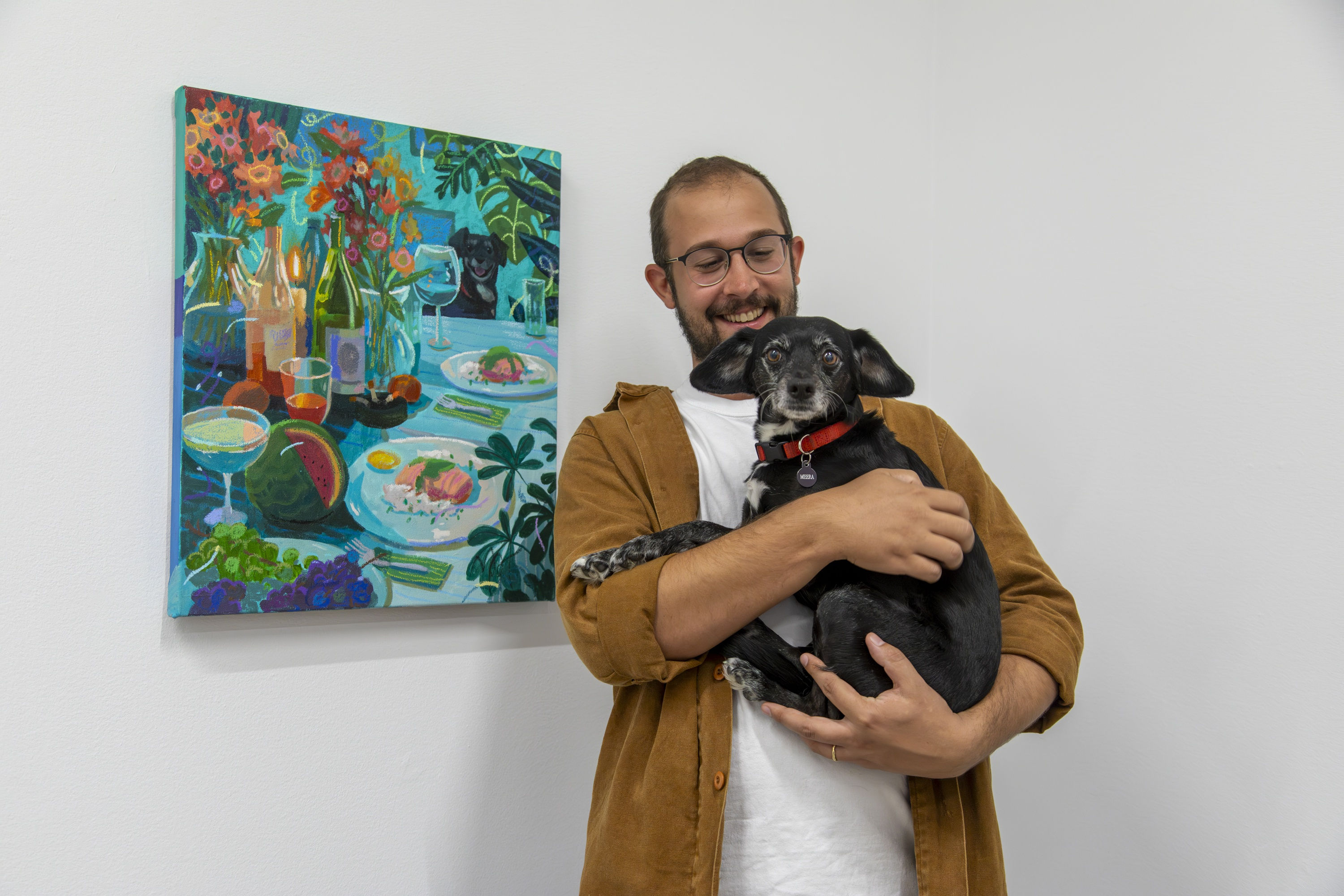 Nicholas Bono Kennedy poses in front of his painting while holding a small black dog.