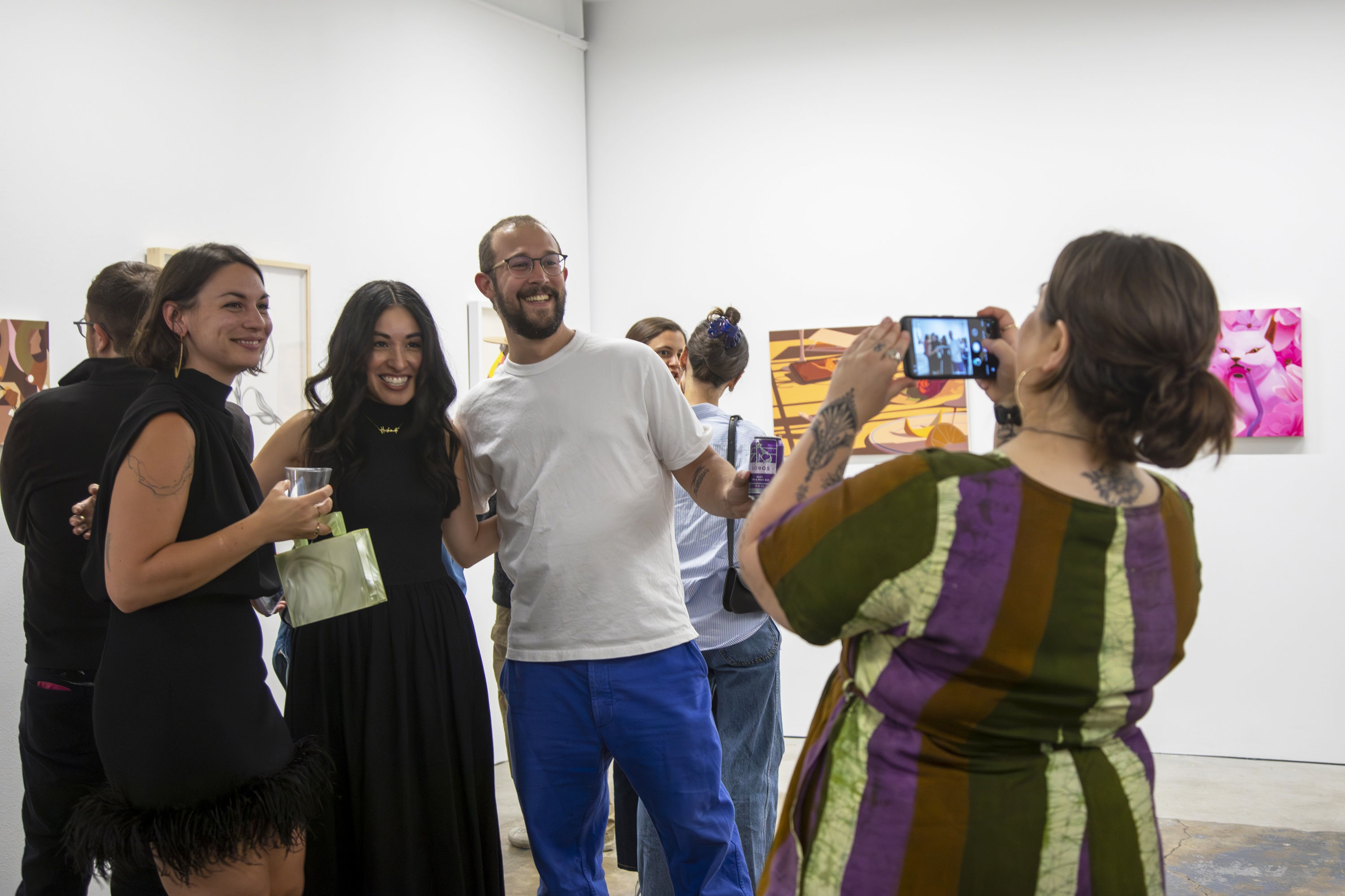 Anna Valdez takes a photo of two artists and Director Jennifer Rizzo in an art gallery at the opening of the 10 Year Anniversary exhibition.