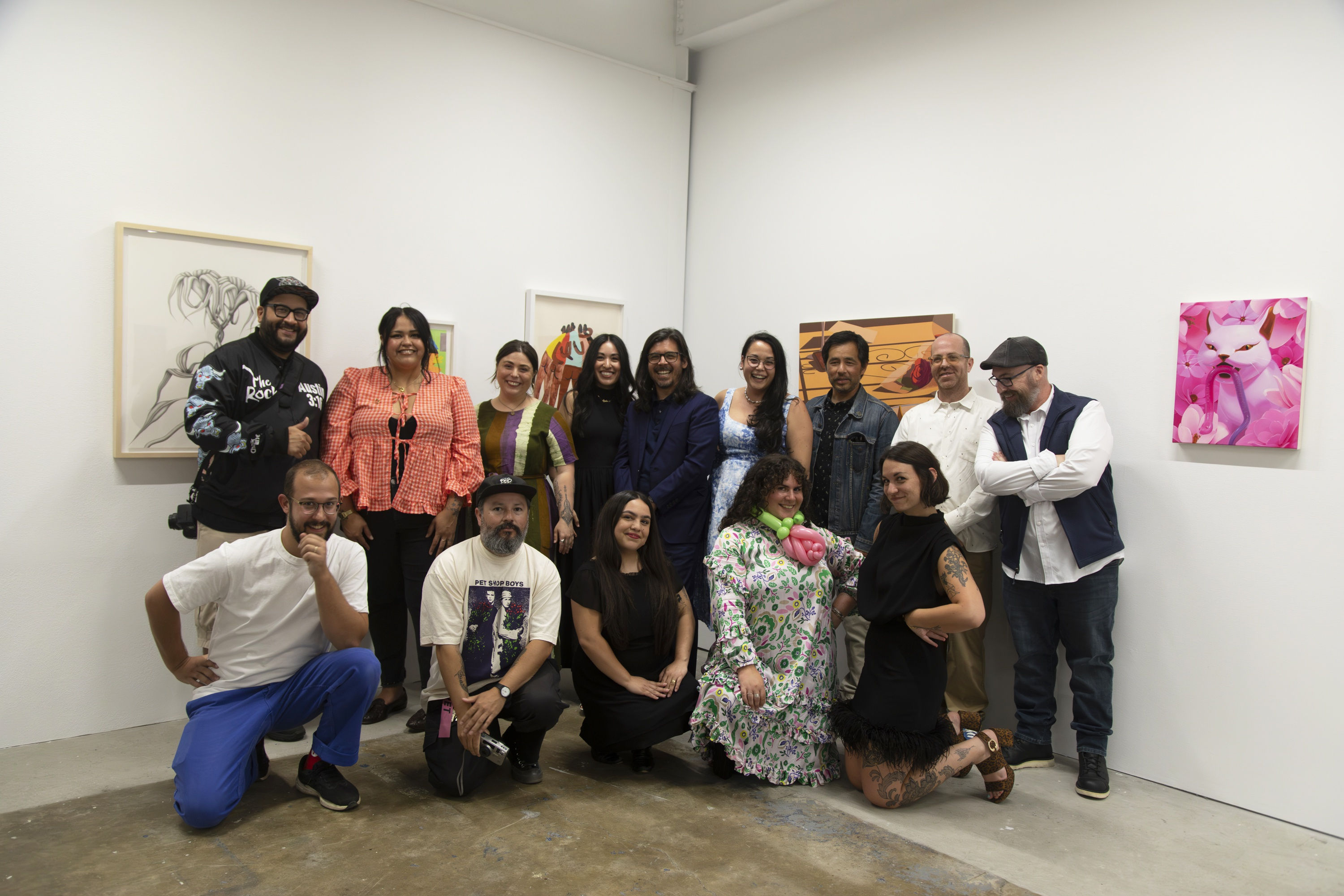 A group of artists and Hashimoto Contemporary staff pose for a group photo in a white wall art gallery with conrete floors and fluorescent lighting.