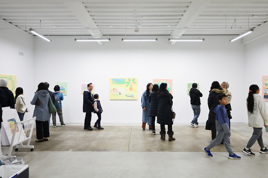A group of people walk around Danym Kwon's solo exhibition A Soft Day. The gallery has white walls and a concrete floor.