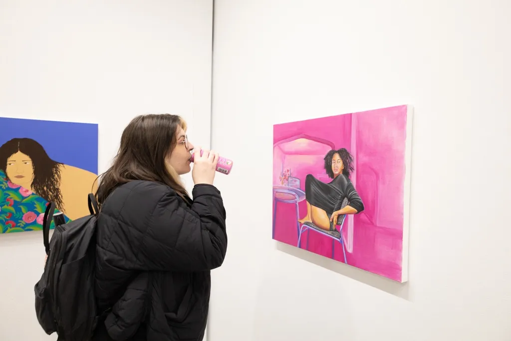 A woman sips a kombucha and looks at Chase Irvin's artwork in a contemporary art gallery. 