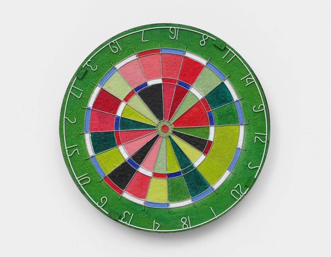 A wall mounted found object sculpture by Acacia Marable, a dartboard painted in red, green, blue and white hues.