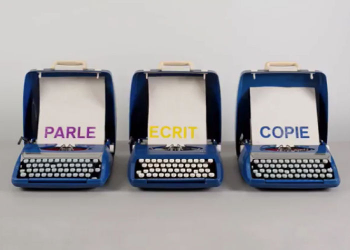 three blue typewriters are installed in a line. each typewriter holds a piece of paper with a single word printed in a different color (in order from right to left: parle, ecrit, and copie)