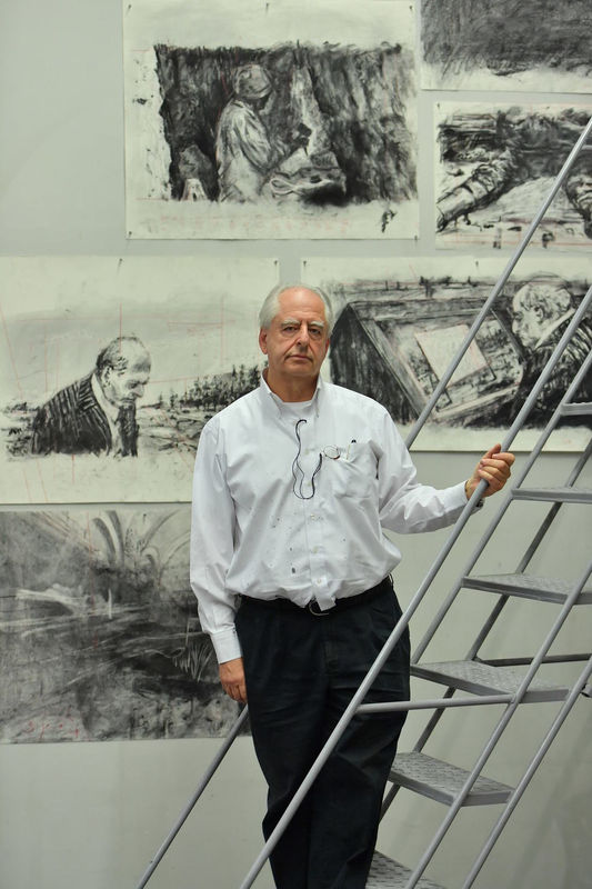 Portrait of William Kentridge standing in front of various charcoal drawings. 