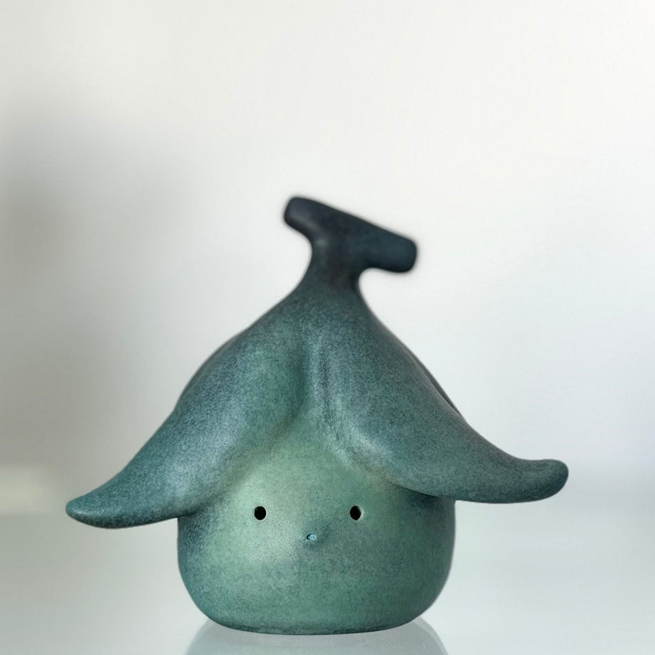 Bronze sculpture of a small round figure with a peeled banana on top of its head