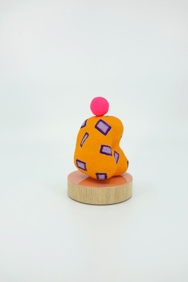 Orange sculpture with purple rectangles painted on it and a pink sphere on top of it