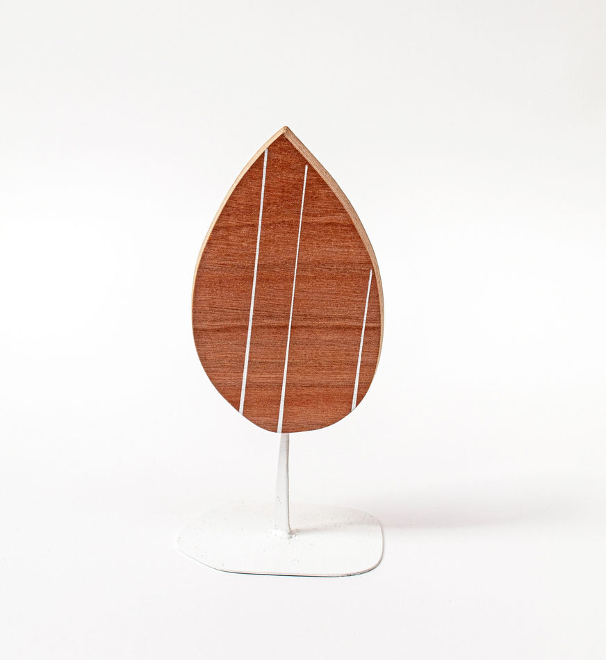 Wooden sculpture of a tear drop shaped piece of wood with three white stripes vertically across it on a white steal stand