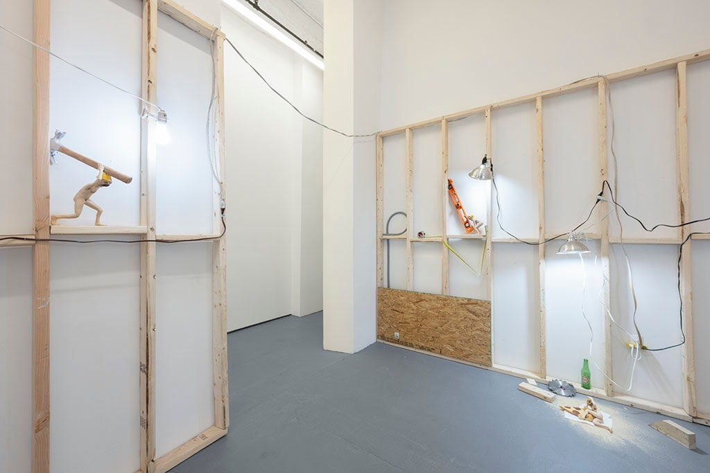 view of entrance to room with white walls, wooden scaffolding, and various dog human sculptures displayed in various scenes