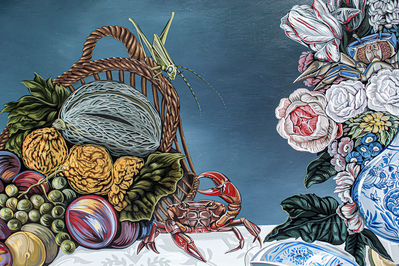 Tablescape painting of two black and white dogs on a table full of decadent food, including a basket of fruit with a grasshopper on it, a giant bouquet of flowers, a bowls of strawberries that has been know knocked over, a plate of giant shrimp, a bowl of whole fish and a white frosted cake that one of the dogs has walked into and gotten frosting all over the table.