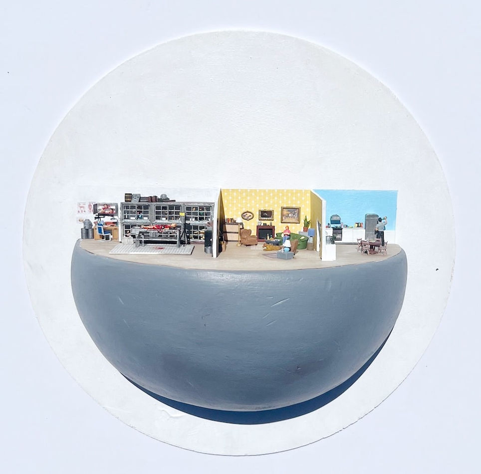 Miniature scene of a house with three rooms. In the first left room is a person naked and bleeding all over on a stretcher. In the middle room is a yellow living room scene with a woman. In the far right room is a man in a kitchen