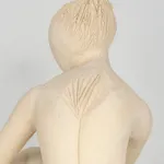 Seated white ceramic figure is looking over her left shoulder with arms draped around her knees which are tucked together.