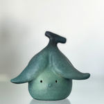 Bronze sculpture of a small round figure with a peeled banana on top of its head