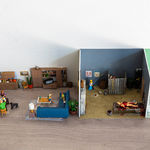 miniature diorama by Abigail Goldman of the interior of house with three rooms, one in which a family is eating dinner and another with people chained and bleeding