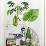 Framed painting of a white bucket and beer bottle with plants sticking out from them