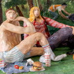 Scenic sculpture of a group of people sitting in a park under palm trees eating in n out on the grass.