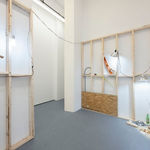 view of entrance to room with white walls, wooden scaffolding, and various dog human sculptures displayed in various scenes