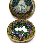 hand-cut watercolor collage in antique cosmetic compact by Shannon Taylor of a large moon with a face and tons of flowers and leaves surrounding it