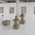Assortment of Japanese stone sculptures in gallery with colorful paintings on back wall.