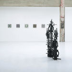 Installation view of Totem with 5 square panel paintings hanging in a horizontal line on the wall behind the sculpture