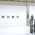 Installation view of Totem with 5 square panel paintings hanging in a horizontal line on the wall behind the sculpture