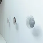 Side view of three reflective disks mounted in a row on a white wall.