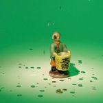 still from video shows spotlight on figurine with happy expression dressed in formal green and orange cap and robes holding a comparatively large shot glass-like cup as rhinestones fall from above on green background