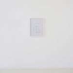 Framed and hung on a white wall; front view of a 5x8 grid of rectangular foil slides, each with unique raised linear designs, in white mounts.