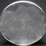 A clear convex disk with etchings set on a dark grey background.