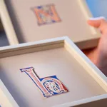 Three decorative medieval illuminated manuscript letters “E” "H", "N" in red, blue, and cream, featuring intricate floral and vine-like patterns inside the letterform, centered on a plain parchment background within a wide margin. From an Atlantic Bible, Tuscany, Italy, 12th century.