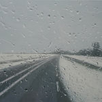 A road leading to a grey-sky horizon with snowy banks on either side of it, seen through a glass screen with water droplets scattered across it. By artist Esther Nienhuis. oil on linen, Rebecca Hossack Art Gallery, London, contemporary artist