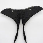 A mosaic sculpture by Leah Shirley in the shape of a moth with black wings. A delicate copper chain extends from the moth's two lower wing edges and stretches to the floor.