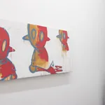 painting by Chris RWK of three red and gold robots hanging on a white gallery wall with a small window and sculpture to its right