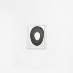 Ted Collier work on paper with a black circle on white background in charcoal framed in white frame hanging on a white wall