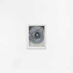 Ted Collier work on paper of vicious chaotic spiral in black in white charcoal framed in a white frame hanging on a white wall