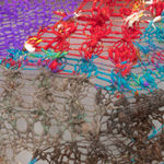 A detail shot of an organic composition with floating geometric accents in multi-colored fibers stretched across a redwood frame as one would stretch a painting. The fibers are knit at varying thicknesses so that in places one can see through the stitches to the wall behind.