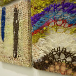 A detail of several knit square compositions, one with arcing black, white, red, and purple colors, the next with strips of blue and brown on a natural background