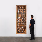 a wooden sculpture hung on a white wall with a figure looking at it