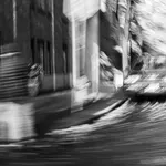 A horizontal black and white architectural photograph by Garrett Gassman featuring a dramatic, high-contrast view of a modern building with sharp angles and deep shadows, printed as an archival photo rag print.