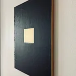 A side-angle shot of "The Fucking Audacity," showing the physical depth of the gold square and how the light catches the metallic texture against the dark canvas.