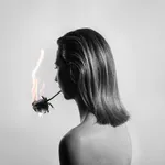 A cinematic black and white photograph by Garrett Gassman featuring a woman in profile holding a rose to her mouth like a cigarette, with smoke drifting from the petals.