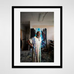 Framed photograph in black wood of an artist Noah Jemison stands with his hands on his hips surrounded by paintings in a loft setting