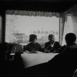Black and white photograph of Senator John F Kennedy, Stephen Smith, and Jacqueline Kennedy having breakfast in a diner booth with their backs to a window while on the campaign trail in Oregon