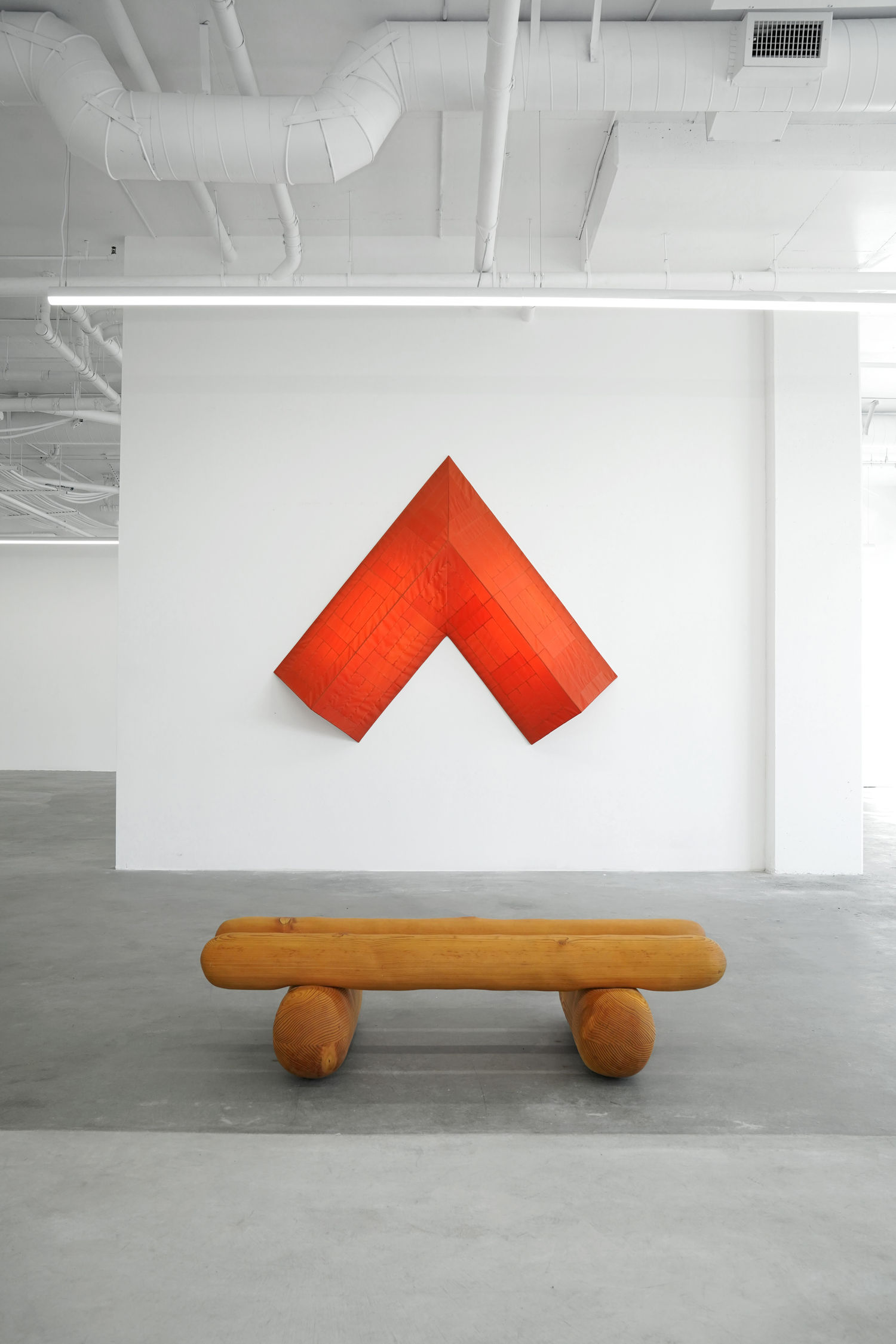 photo of the gallery with a wooden bench by Ryan Belli and a red light intstallation shaped like a red arrow