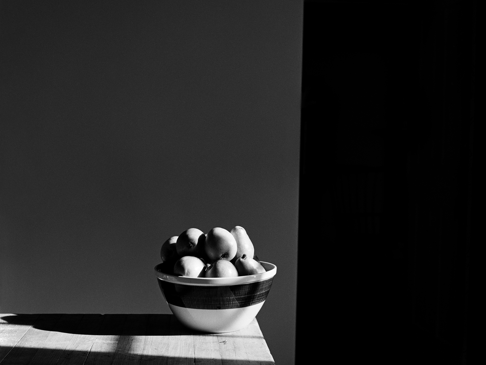 A bowl of pears sits in a beam of sunlight in this black and white graphical photograph.