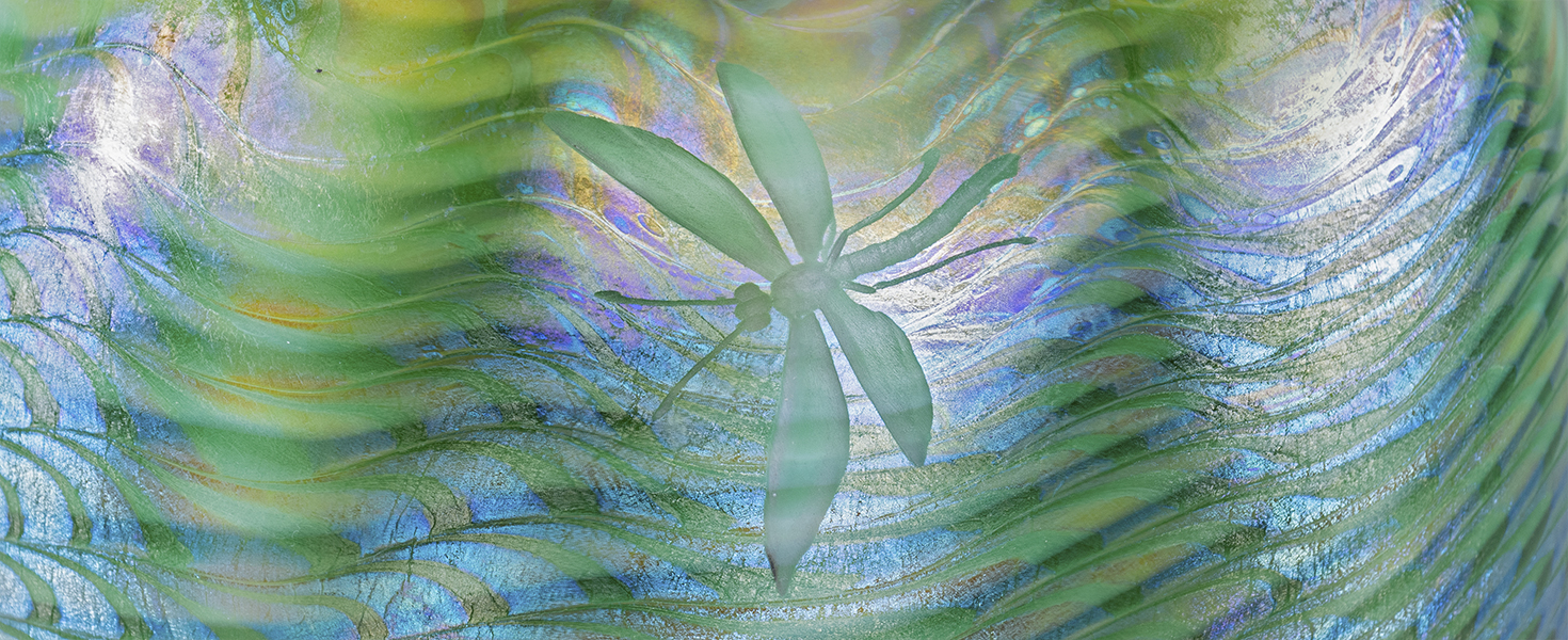 a detail of a blown favrile glass Tiffany lamp shade, the iridescent blue and green glass decorated with a "wave" motif, with an intaglio or wheel-carved dragonfly